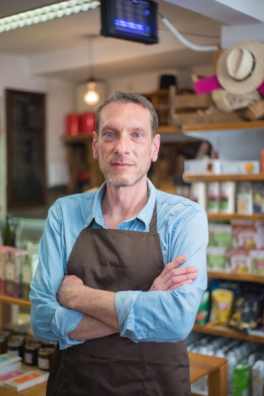 Confident male shop owner with arms crossed in a rustic village store.